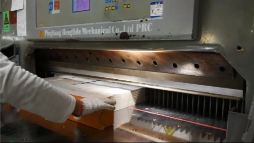 Worker operating an industrial paper cutting machine for custom printed products